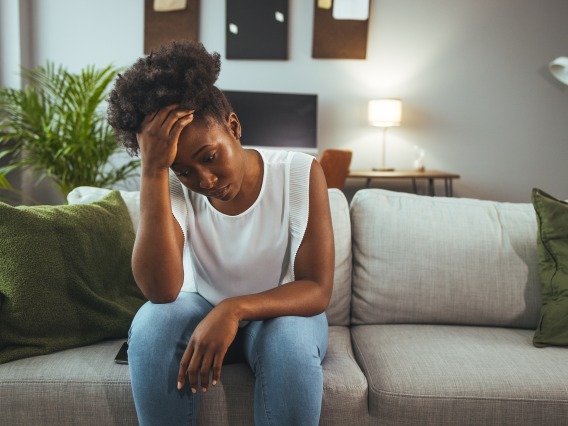 woman sitting on couch with hand on head looking troubled