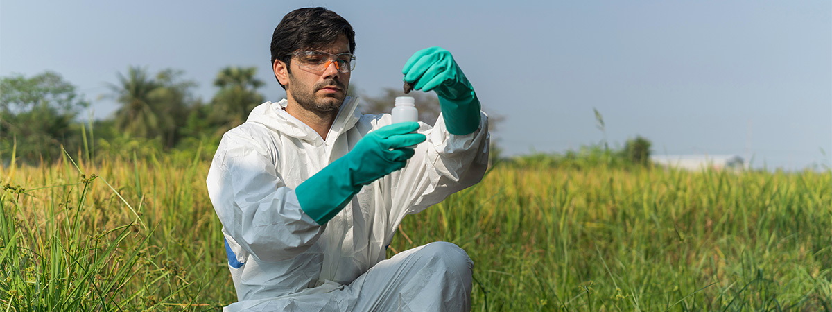 technician in overall protective suit collecting samples of soil